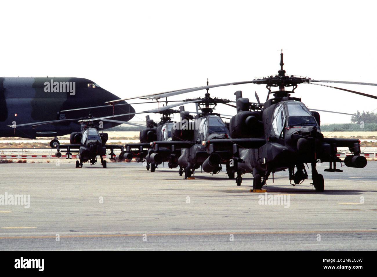 A C-5A Galaxy aircraft taxis past a row of AH-64 Apache helicopters during Operation Desert Shield. Subject Operation/Series: DESERT SHIELD Country: Saudi Arabia (SAU) Stock Photo