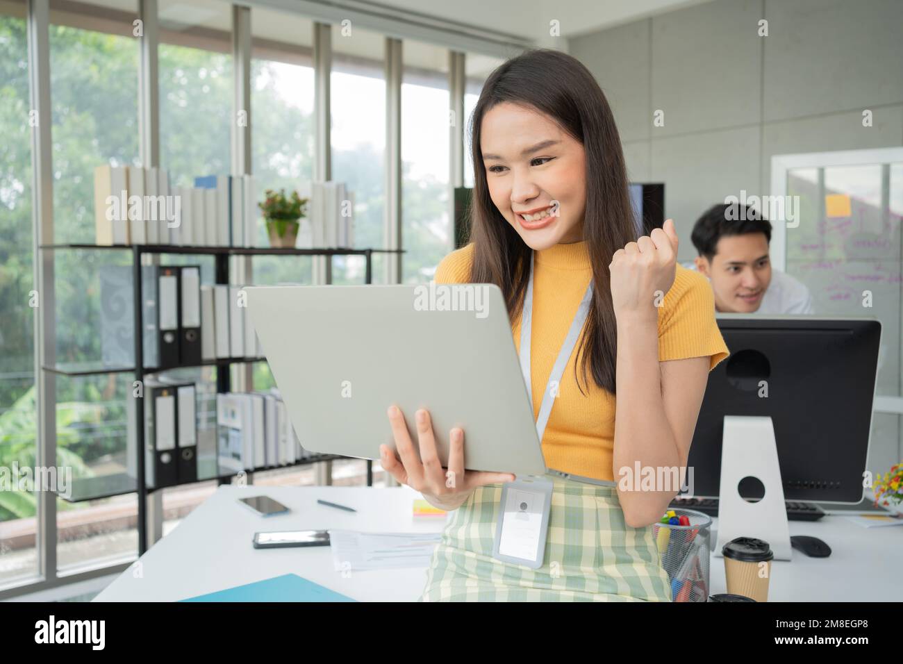 Young Asian Happy Businesswoman or intern using Computer in Modern Office background is Colleagues discuss with new startup project Idea. Empowered Di Stock Photo