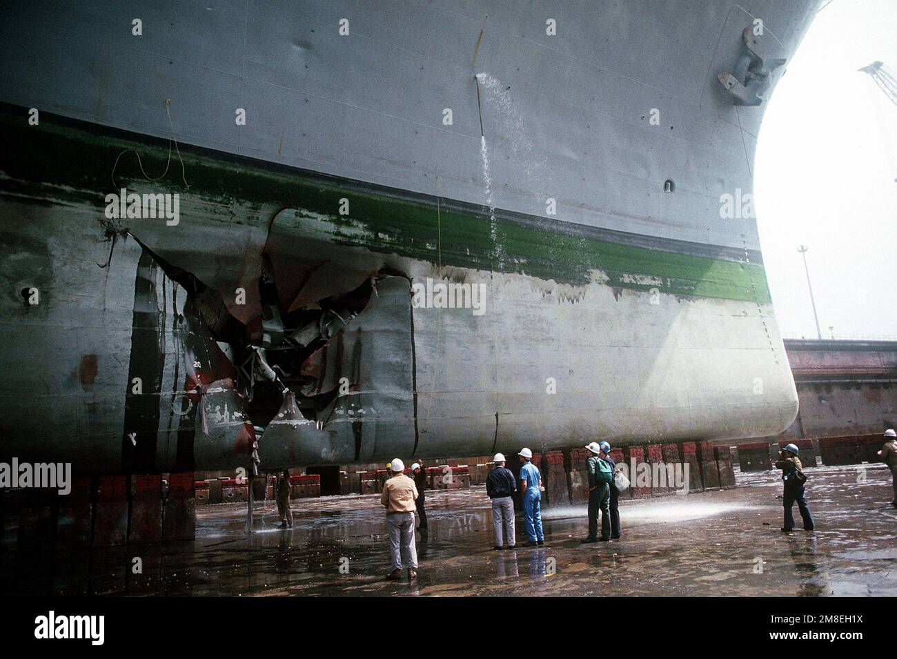 Navy personnel inspect damage to the hull of the amphibious assault ...