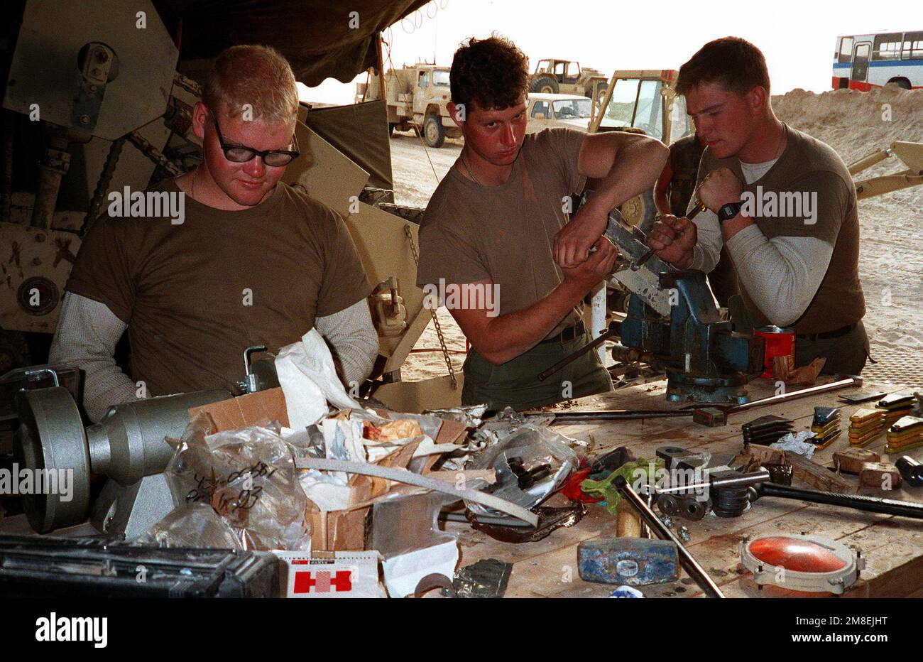 Timothy Lamm, left, a Seabee from Naval Mobile Construction Battalion 5 (NMCB-5), uses a grinding wheel as Seabees John Stevenson, center, and John Redlewski try to free a bolt in a workshop at a camp under construction in northern Saudi Arabia during Operation Desert Storm. Subject Operation/Series: DESERT STORM Country: Saudi Arabia (SAU) Stock Photo