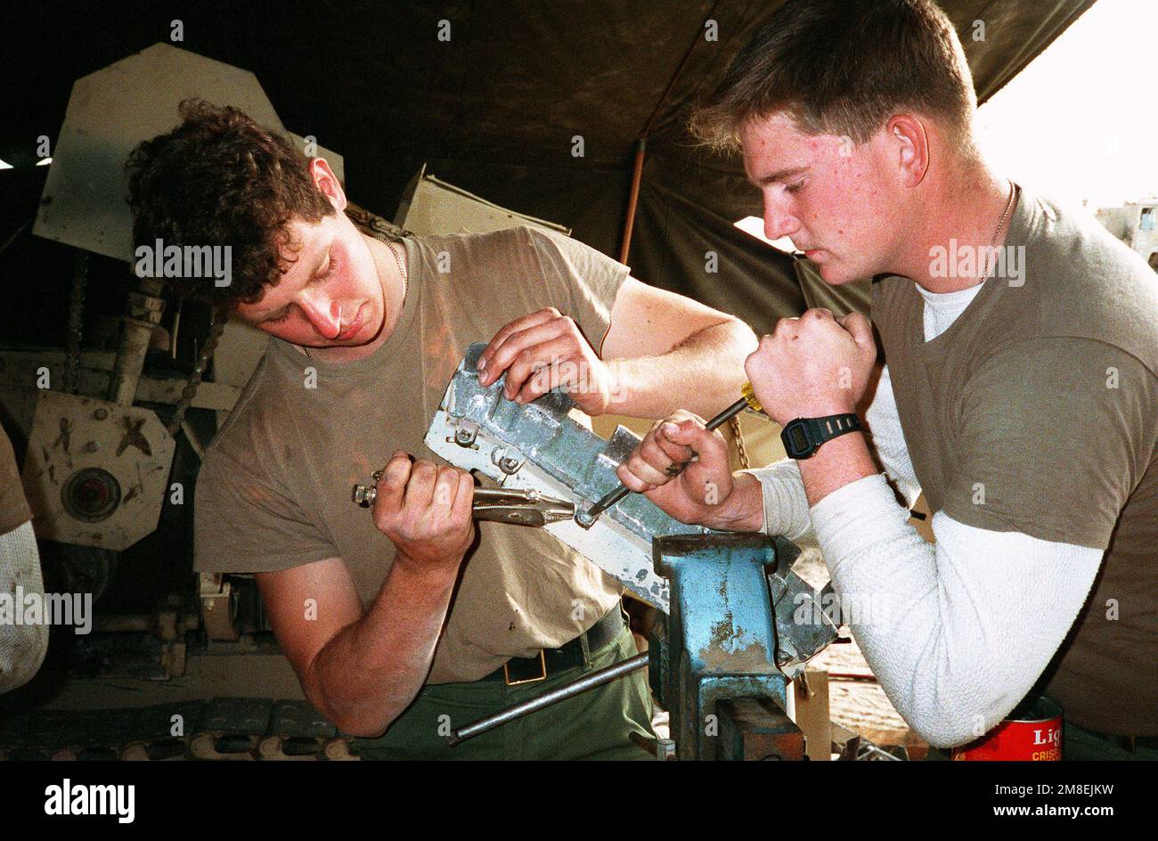 John Stevenson, left and John Redlewski, Seabees with Naval Mobile Construction Battalion 5 (NMCB-5), try to free a bolt on a piece of equipment in a workshop at a camp under construction in northern Saudi Arabia during Operation Desert Storm. Subject Operation/Series: DESERT STORM Country: Saudi Arabia (SAU) Stock Photo