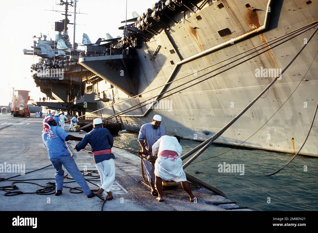 Dock workers secure mooring lines from the aircraft carrier USS SARATOGA (CV-60), as it pulls in to the pier during Operation Desert Storm.. Subject Operation/Series: DESERT STORM Base: USS Saratoga(CV 60) State: Jeddah Country: Saudi Arabia(SAU) Stock Photo