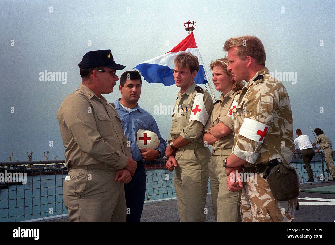 SENIOR CHIEF Hospital Corpsman W. C. Tutcher, left, and Hospital Corpsman 3rd Class Frank J. Chaves, second from left, compare notes with Dutch medical personnel on the deck of the Dutch fast combat support ship HNLMS ZUIDERKRUIS (A832) while the ship is in port during Operation Desert Storm. Tutcher and Chaves serve aboard the guided missile frigate USS MCINERNEY (FFG-8). Subject Operation/Series: DESERT STORM Country: Bahrain (BHR) Stock Photo