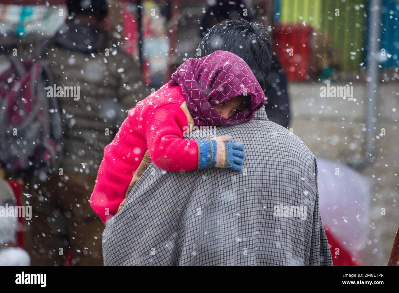 A Kashmiri man carries his child as he walks through a street amid ongoing heavy snowfall on the outskirts of Srinagar. At least two labourers killed on Thursday after an avalanche hits high-altitude area in central Kashmir's Sonamarg. Most parts of Kashmir received fresh snowfall that leading to the closure of Kashmir capital's main highway that connects disputed region with the rest of India. Meanwhile airport authorities suspended all flight operations till further notice due to continuous snowfall and low visibility. Stock Photo