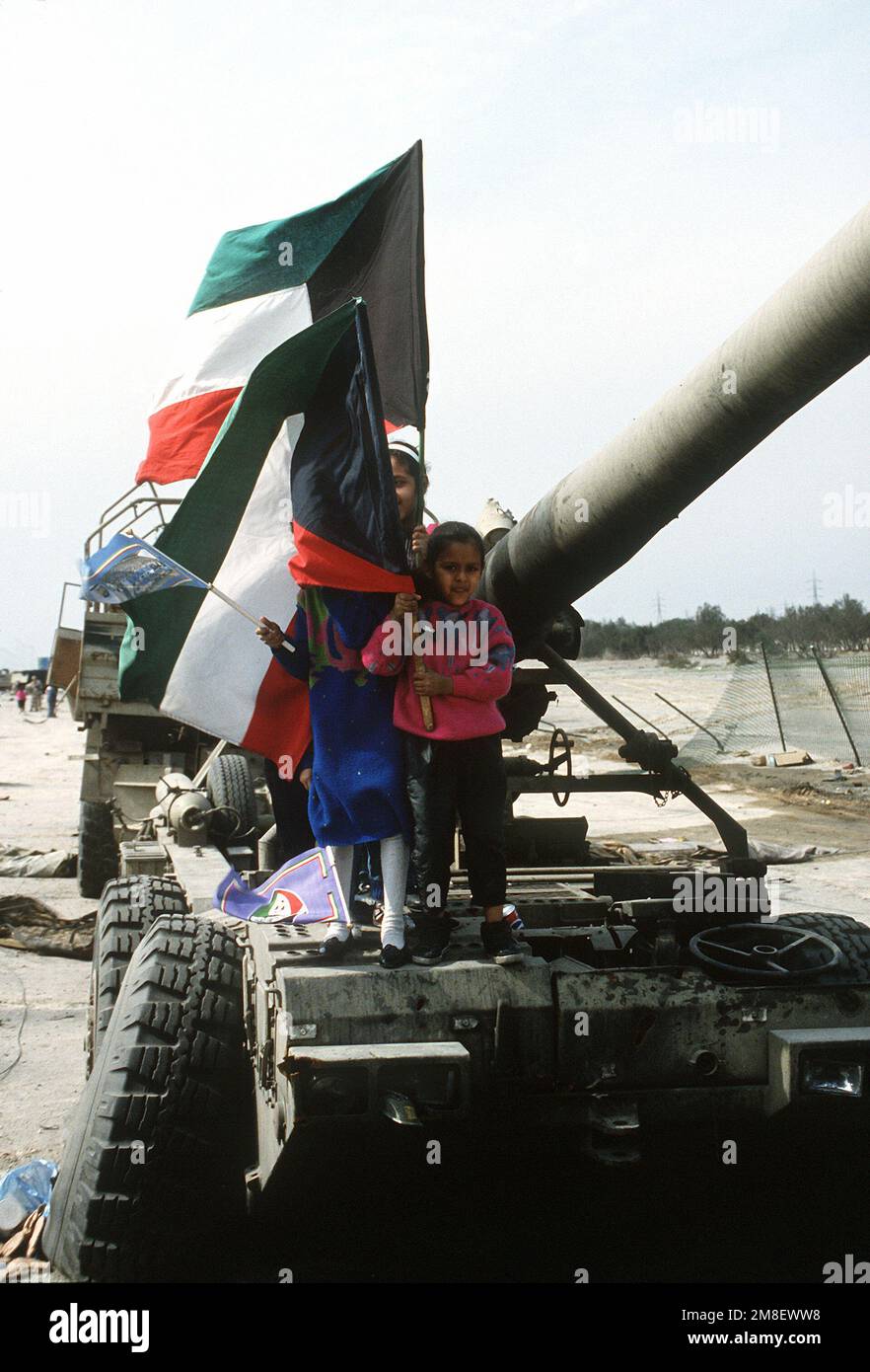 Children waving Kuwaiti flags stand on a large gun during the