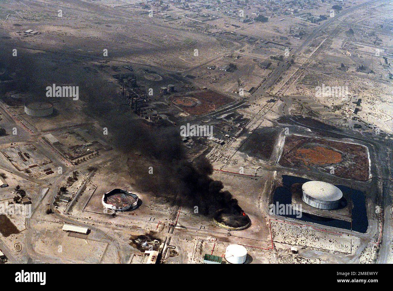 An oil storage tank at a refinery that was attacked by coalition aircraft during Operation Desert Storm continues to burn days after the air strike. The refinery is located approximately seven miles west of the Kuwaiti border.. Subject Operation/Series: DESERT STORM Country: Iraq(IRQ) Stock Photo