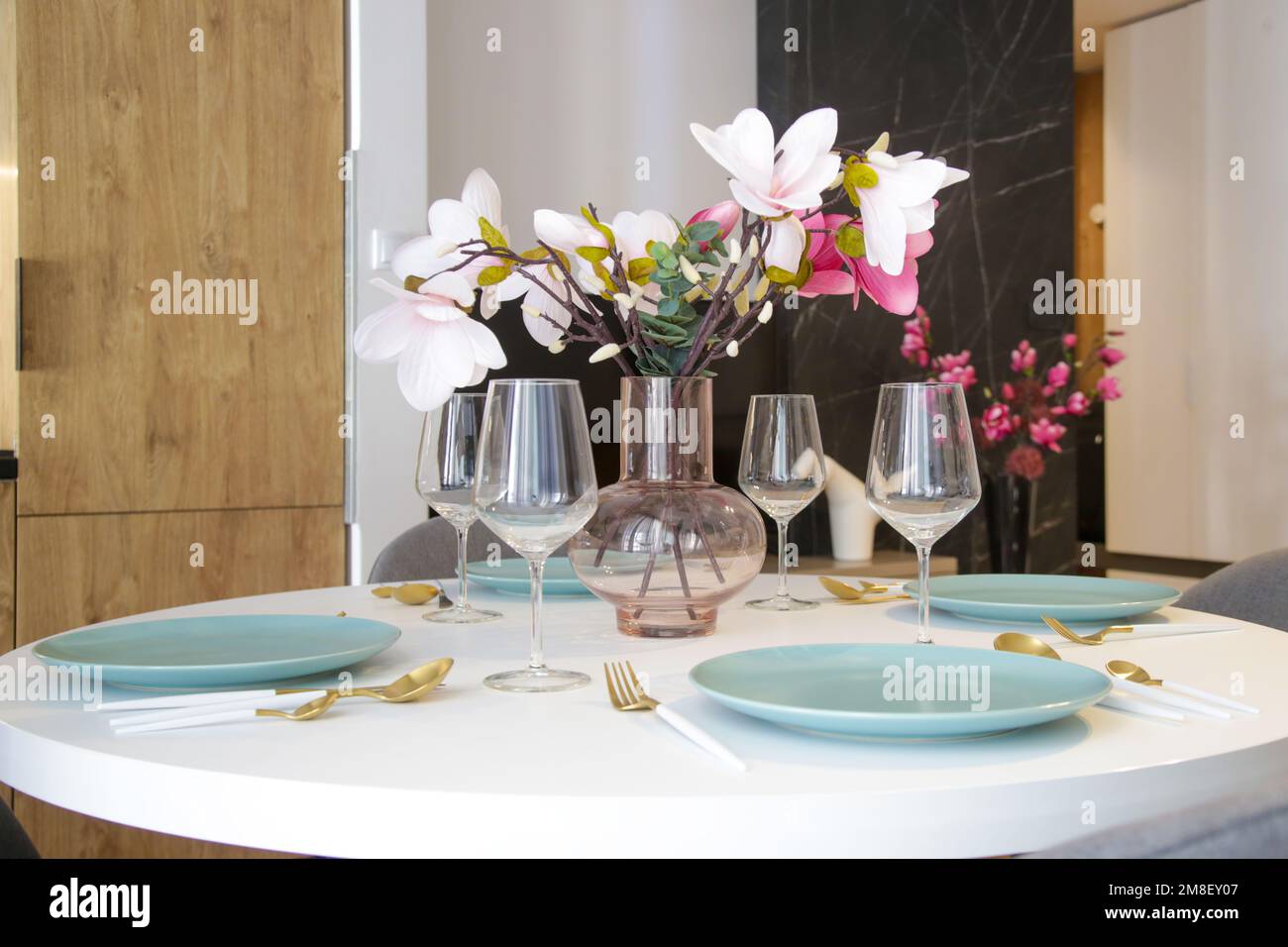Round dining table in modern apartment, table setting with flowers for