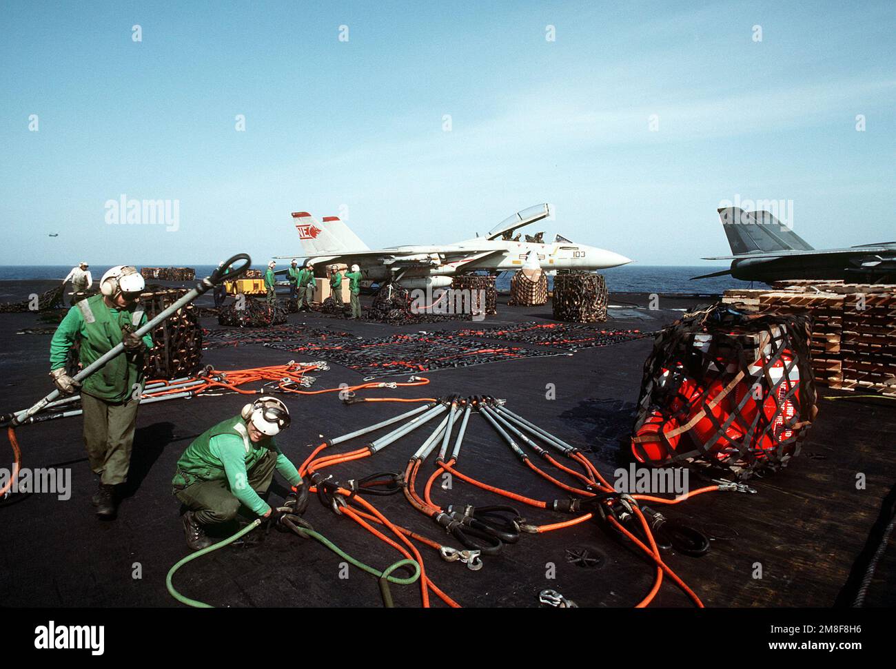 Flight deck crewmen arrange hoisting slings and unload cargo nets aboard the aircraft carrier