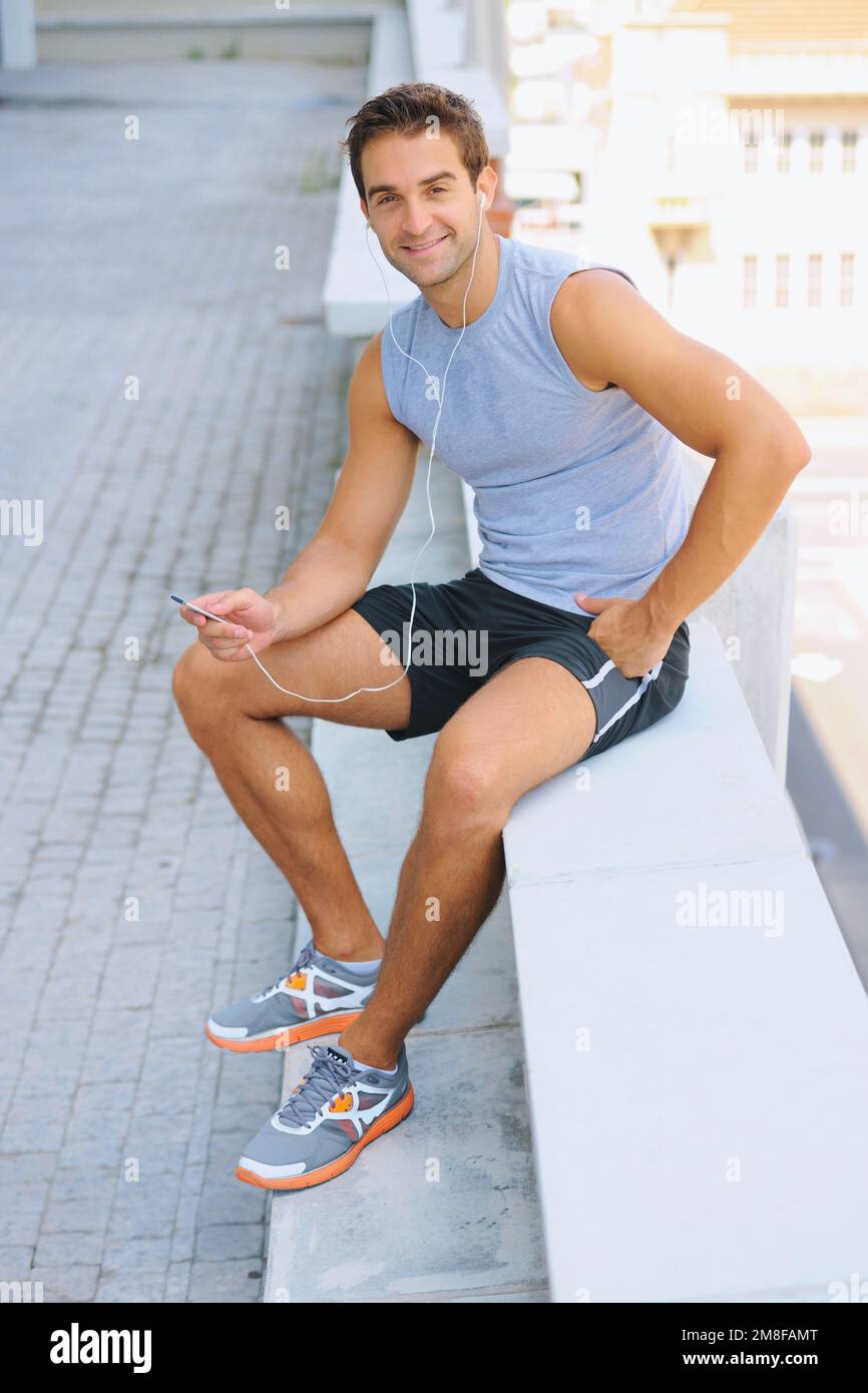 Taking time to catch his breath. Handsome young jogger sitting down and taking a break - portrait. Stock Photo