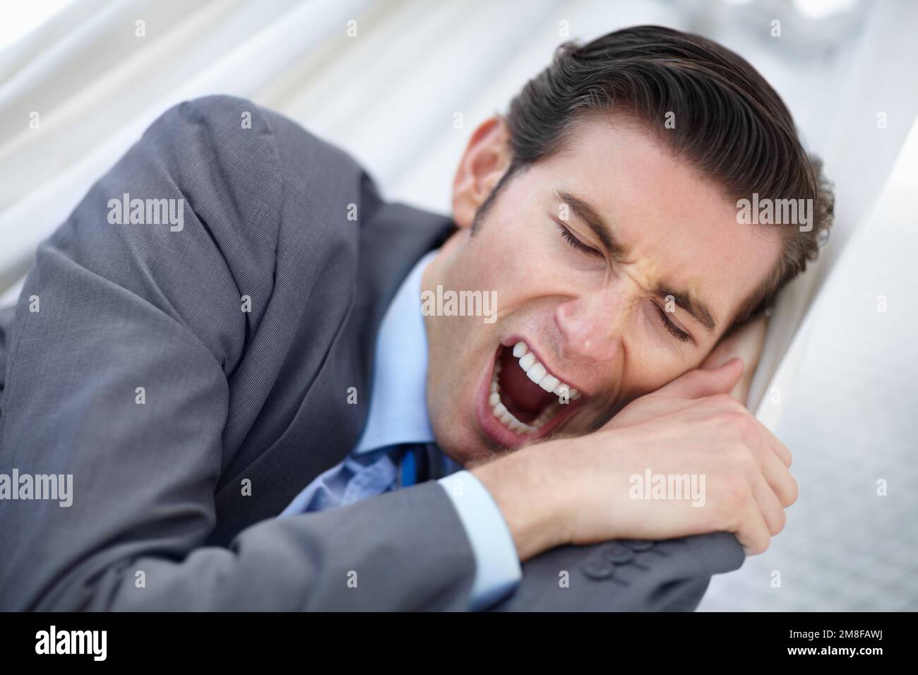 In need of a vacation. A young businessman yawning while lying on a hammock. Stock Photo
