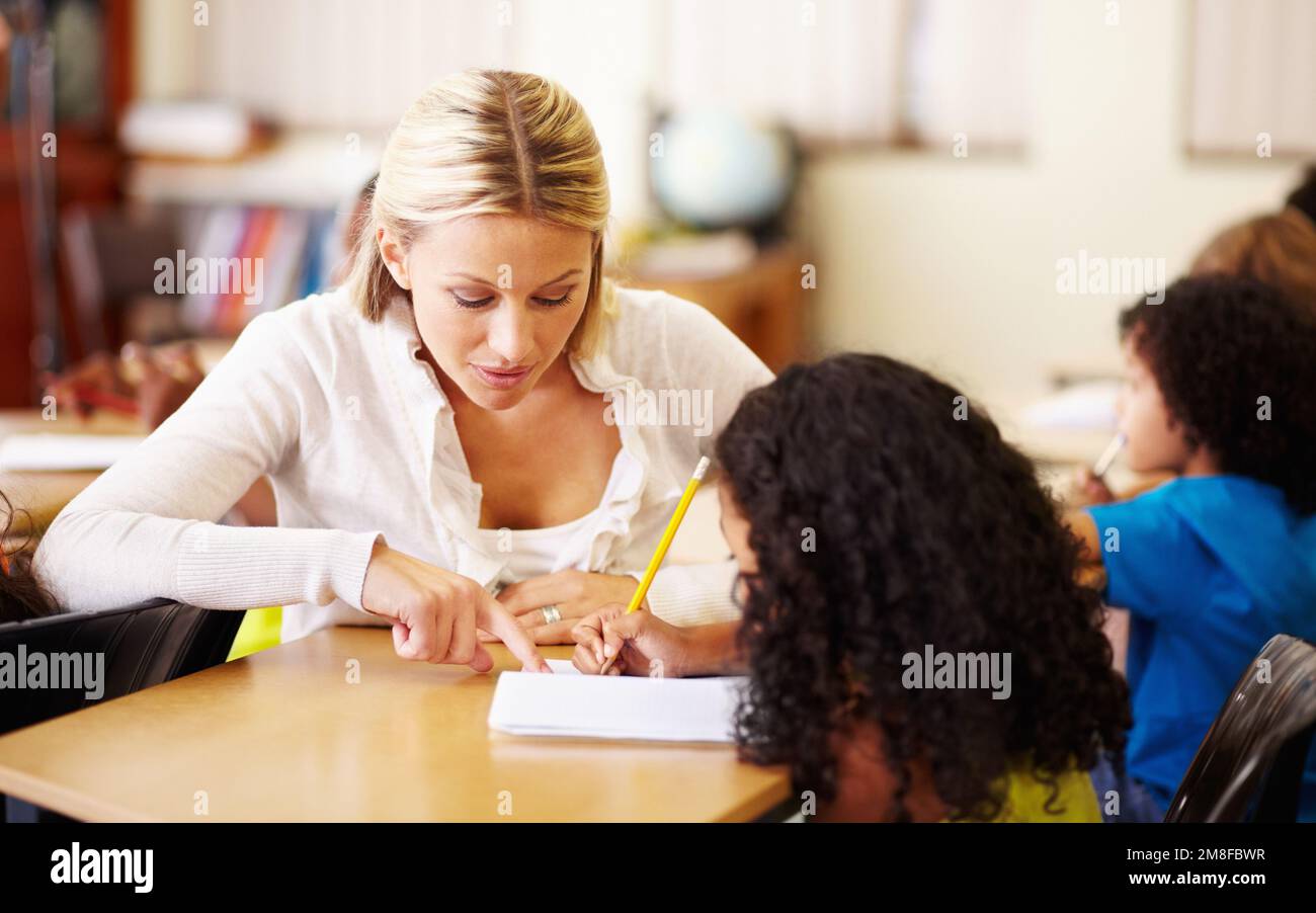 Showing them how to do the sums. A young teacher helping children with ...