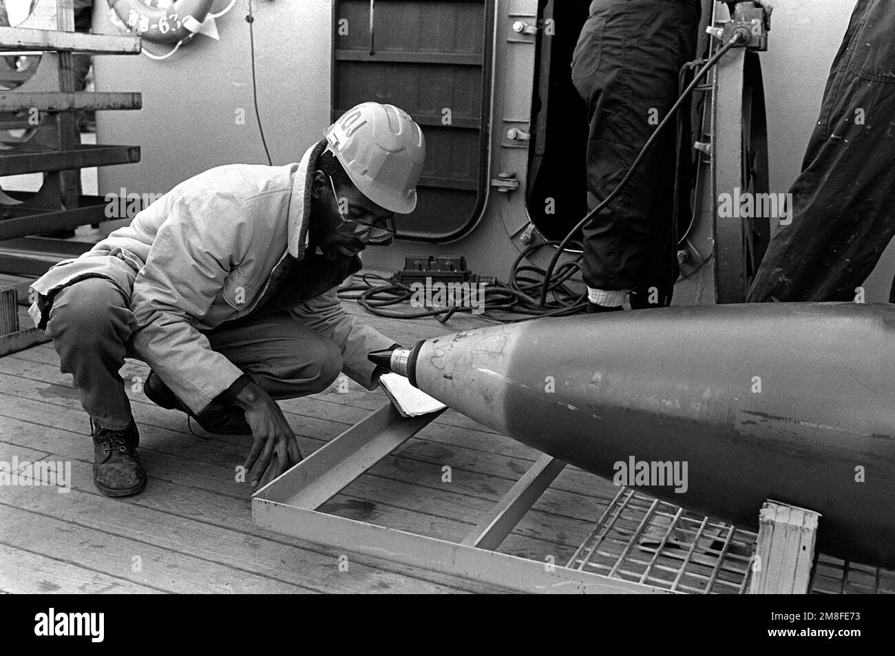 a-civilian-worker-inspects-the-fuze-of-a-16-inch-projectile-on-the-deck