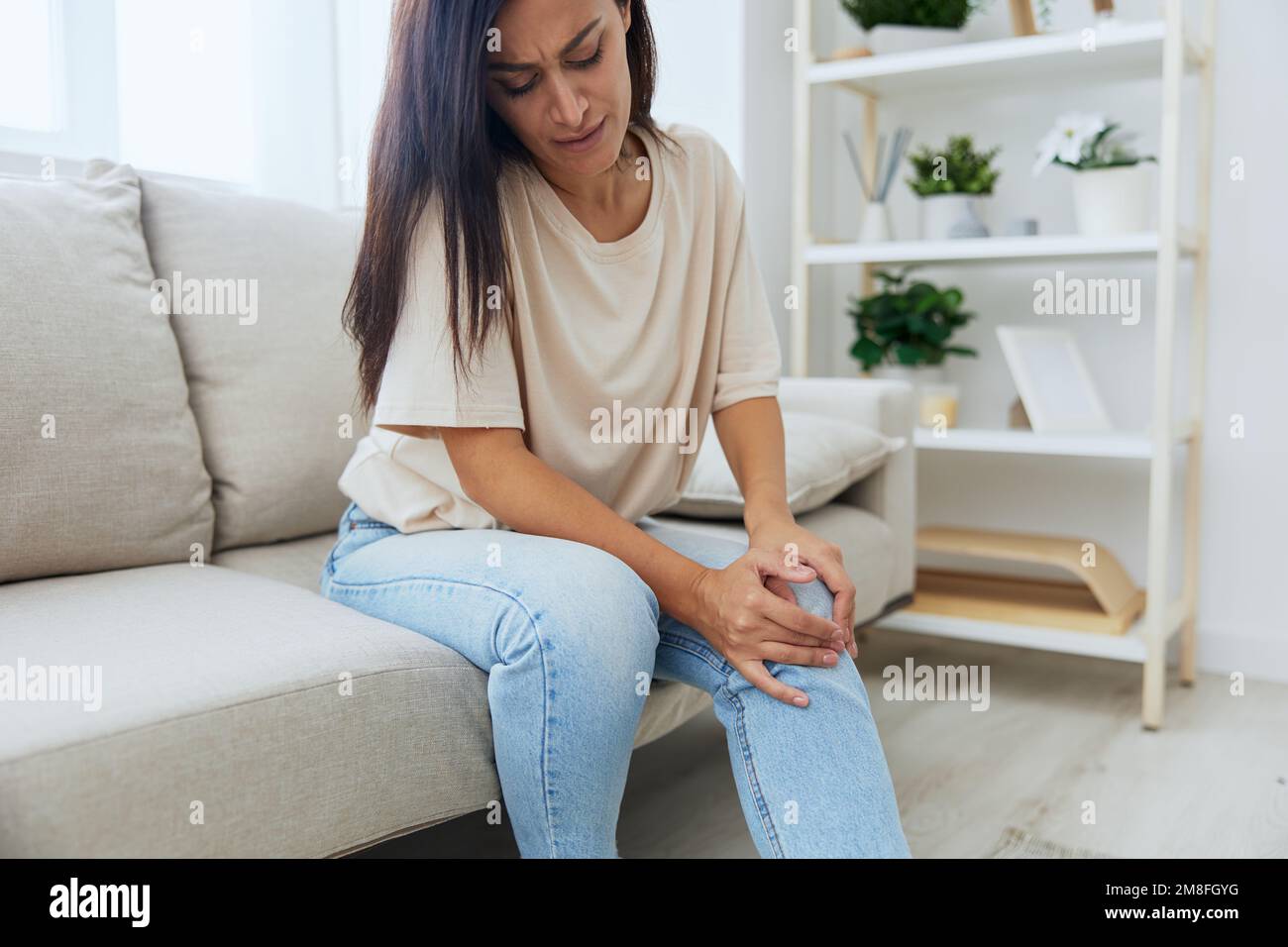 Woman sitting on the couch at home leg and foot pain, sprain and muscle