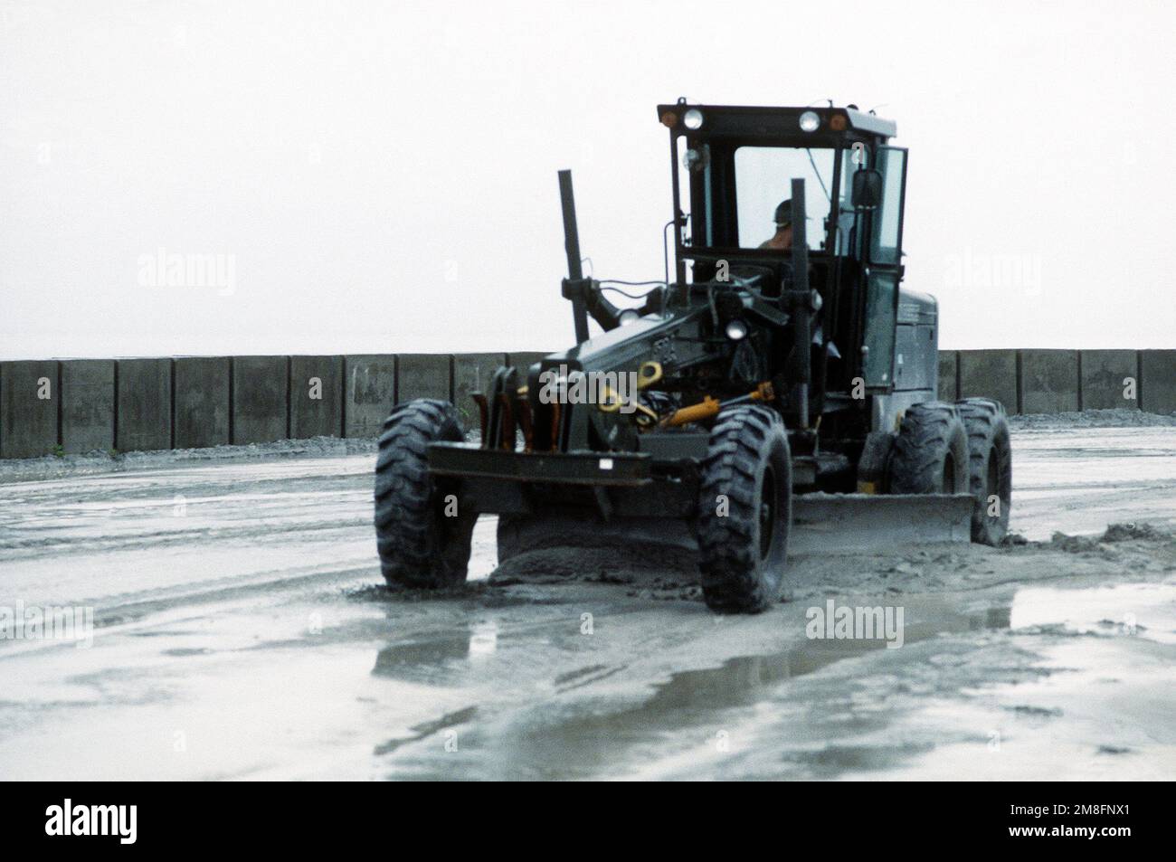 A Seabee uses a John Deere 670A motor grader to clear volcanic ash and ...