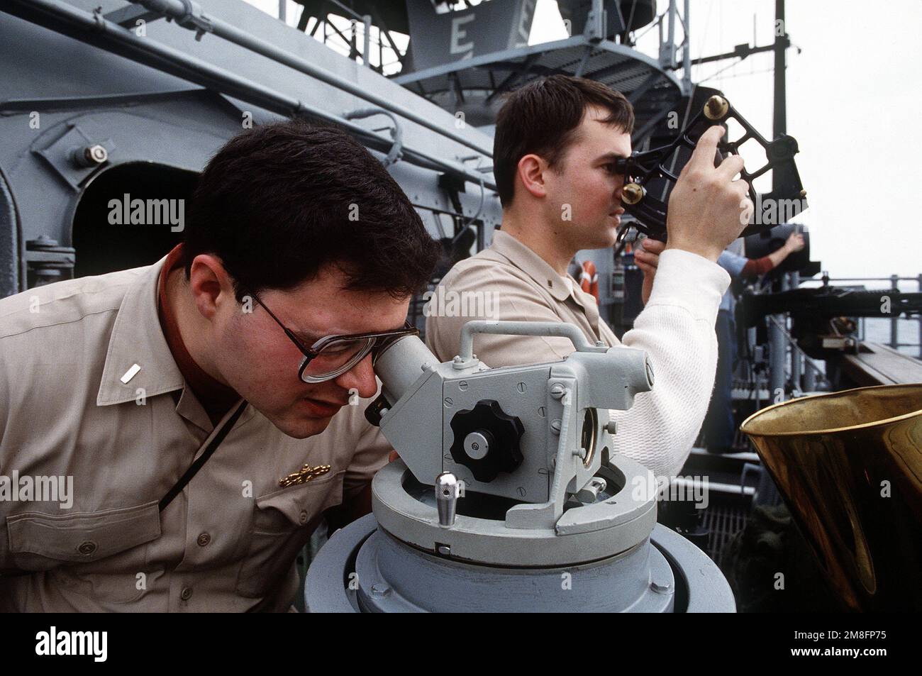 Two officers use a telescopic alidade, foreground, and a sextant to determine the position of the guided missile cruiser USS BUNKER HILL (CG-52) during Operation Desert Storm. Subject Operation/Series: DESERT SHIELD Country: Persian Gulf Stock Photo
