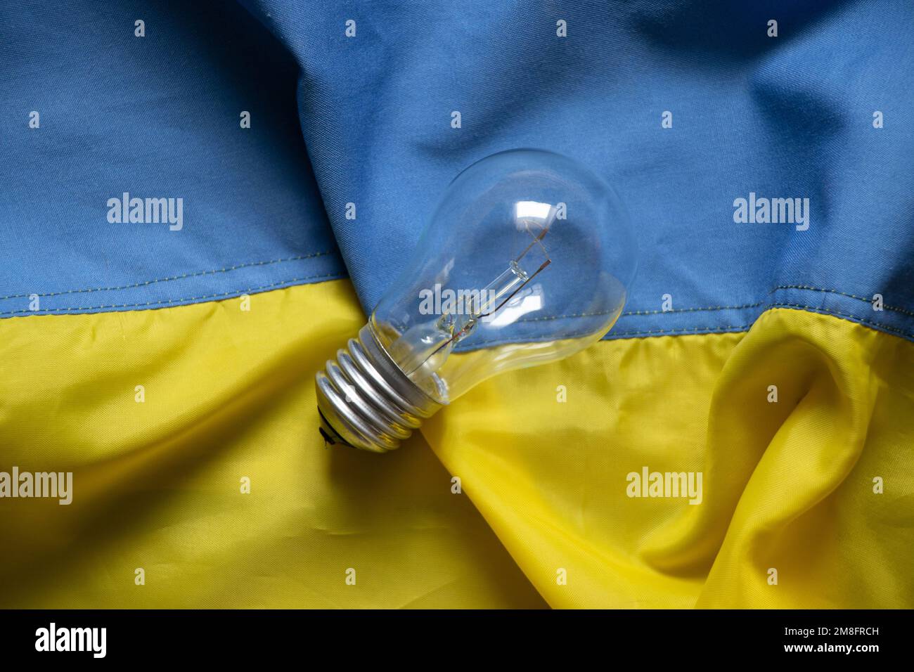 An incandescent lamp lies on the flags of Ukraine, people without light