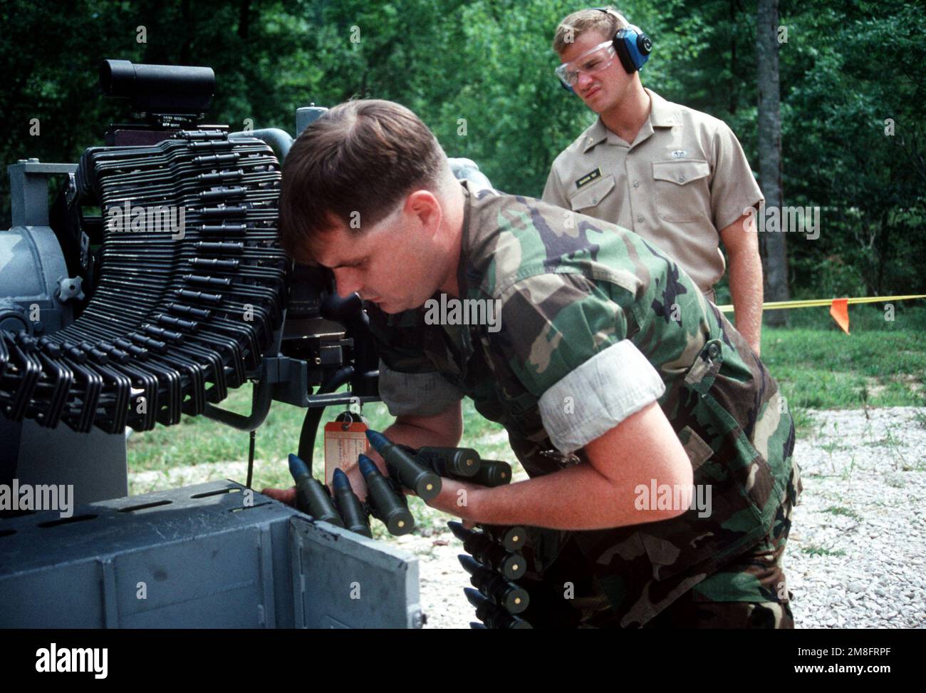 A petty officer places a fresh belt of ammunition in the magazine of a Mark 38 25mm gun system as a visiting midshipman from the U.S. Naval Academy waits to fire the weapon. Base: Naval Weapons Sup Cen, Crane State: Indiana(IN) Country: United States Of America (USA) Stock Photo