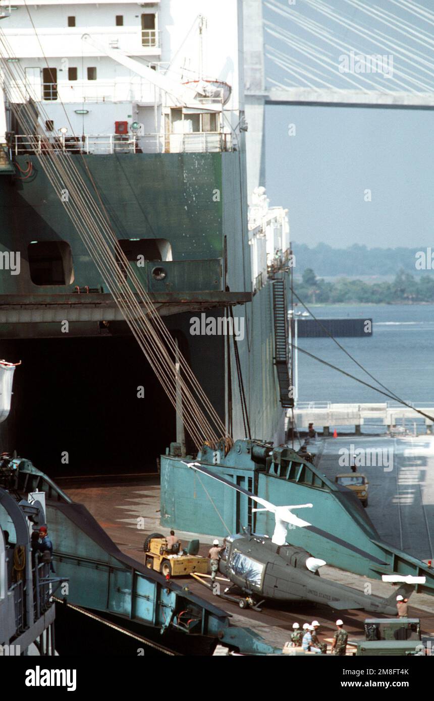 A tow tractor pulls a UH1H Iroquois helicopter up the stern ramp of