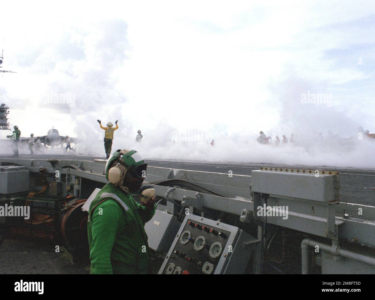 Flight deck crewmen work amidst the steam from a catapult launch on the