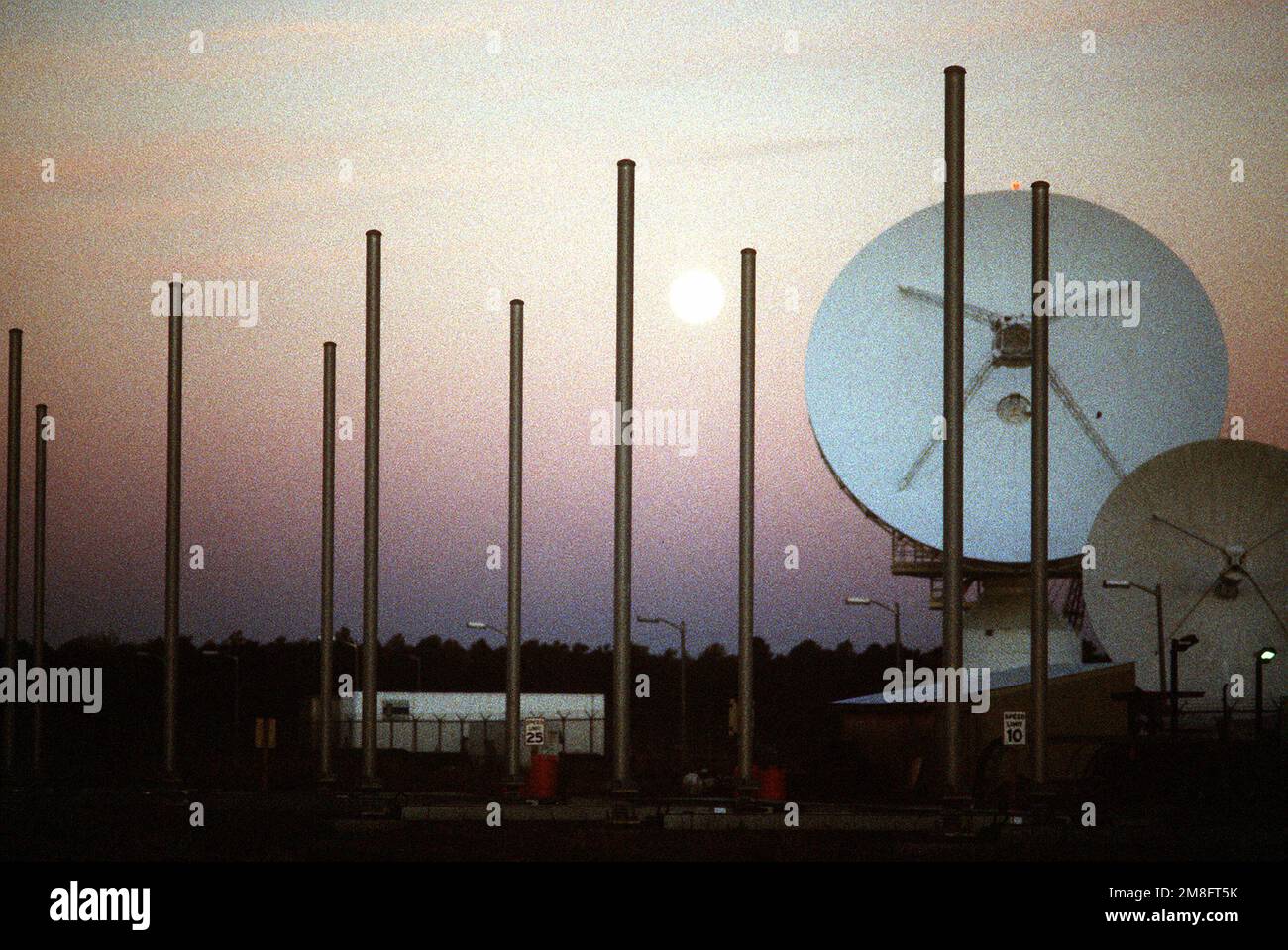 A full moon rises behind a pair of satellite communications dishes at
