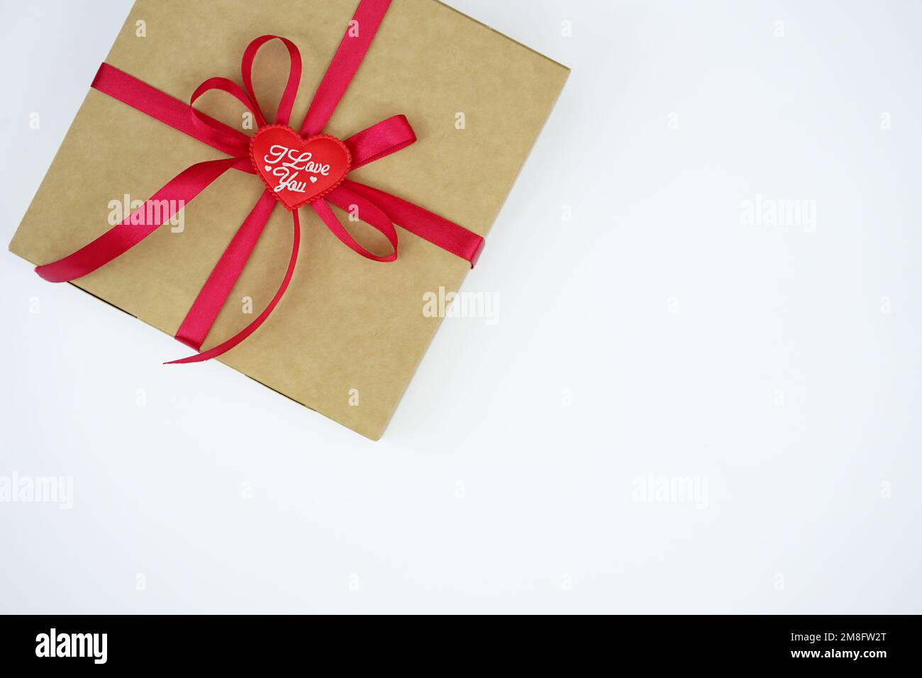 A gift wrapped in a kraft box with a red satin ribbon was isolated on white. The concept of a gift, New Year, Valentine's Day, Birthday, greetings Stock Photo
