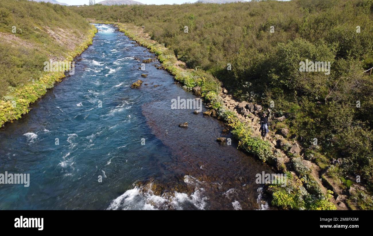 A drone shot of a hiker standing on the rocks on the Bruara River bank on a sunny day, Iceland Stock Photo