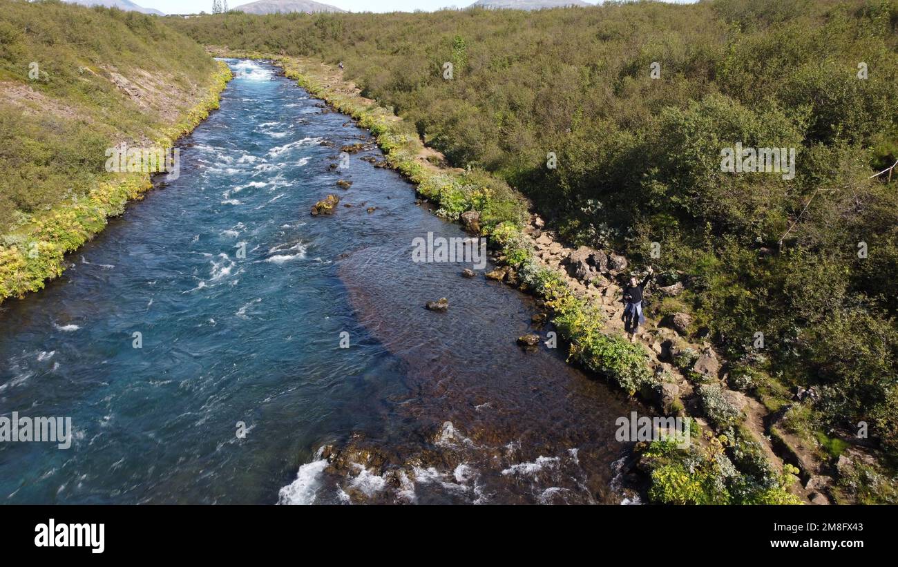 A drone shot of a hiker standing on the rocks by the Bruara River waving to the camera on a sunny day Stock Photo