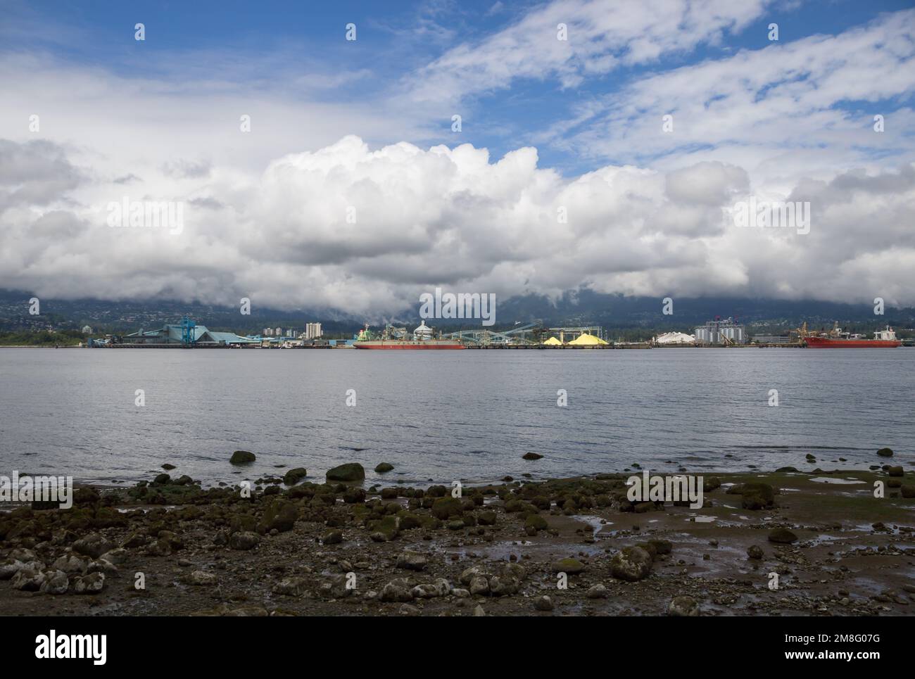 North Vancouver - mountains, bay, Cargo warehouse - industrial port, cargo ship. beautiful clouds and the sea. Travel in the summer. Stock Photo