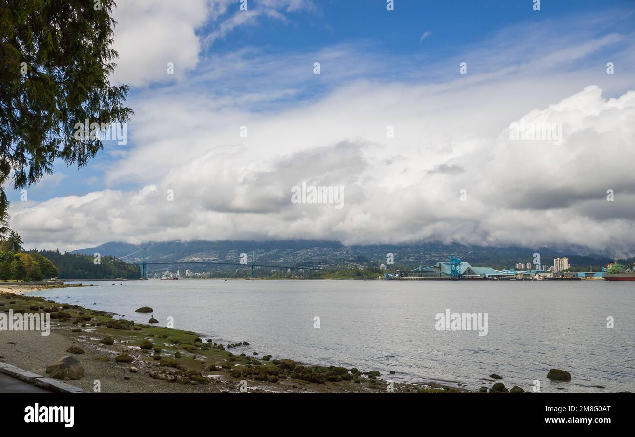 North Vancouver - mountains, bay, Cargo warehouse - industrial port, cargo ship. beautiful clouds and the sea. Travel in the summer. Stock Photo