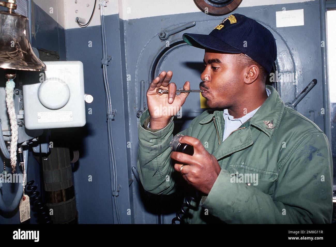 A boatswain's mate uses a boatswain's pipe to make a call over the 1MC circuit aboard the