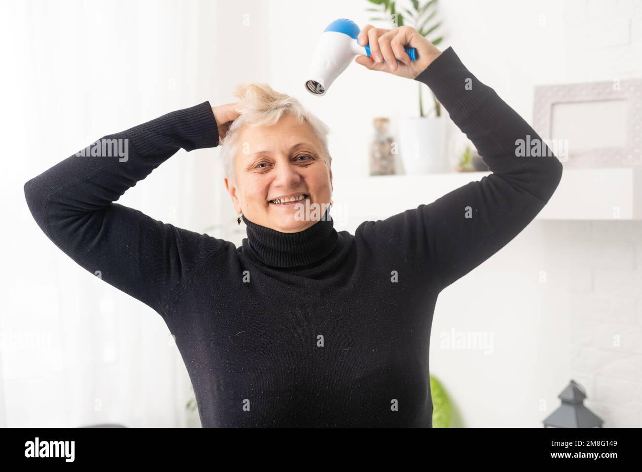 senior woman drying her hair with a hair dryer Stock Photo - Alamy