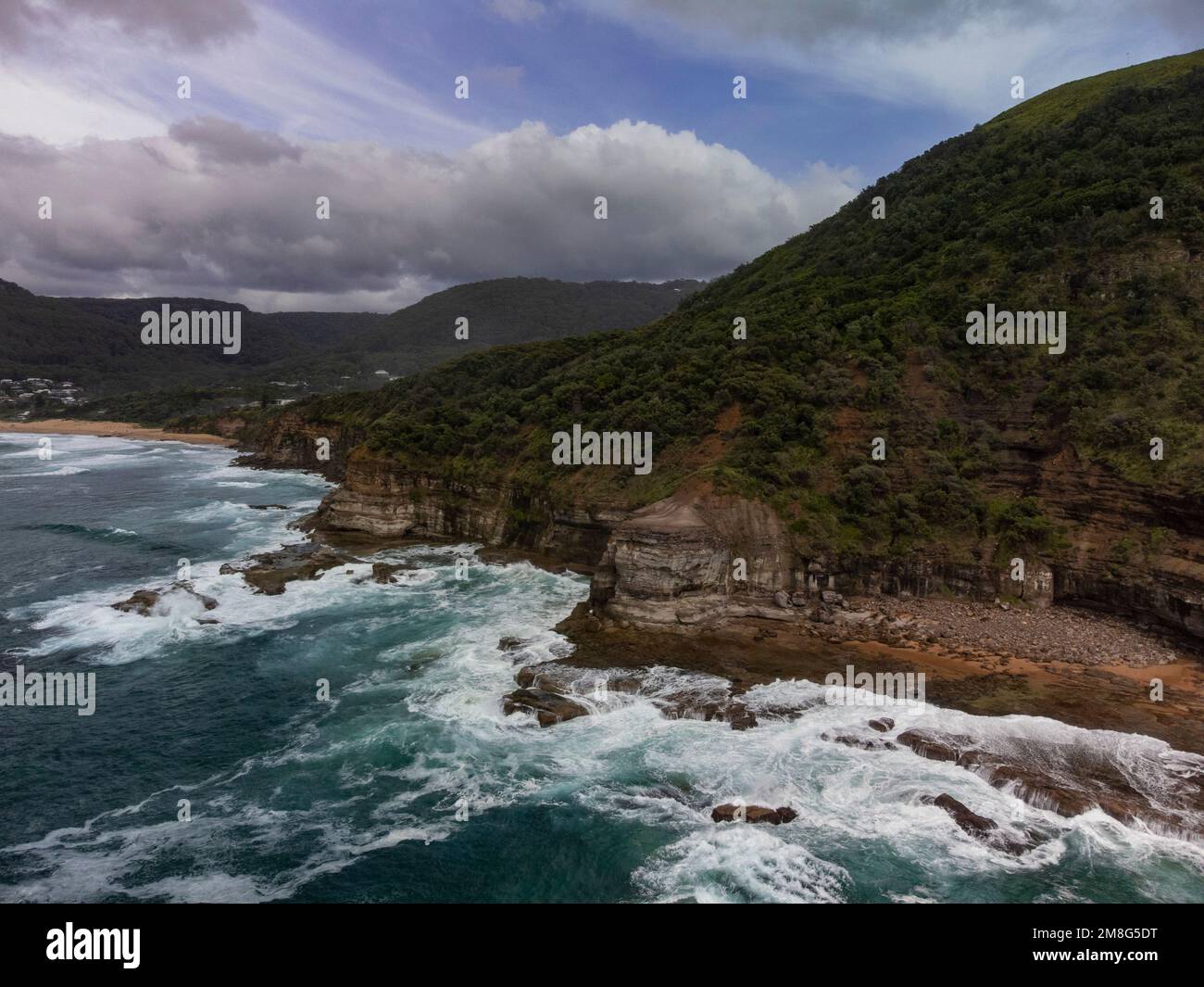A scenic view of evergreen cliffs surrounding the beautiful ocean in Stanwell Park beach, Australia Stock Photo