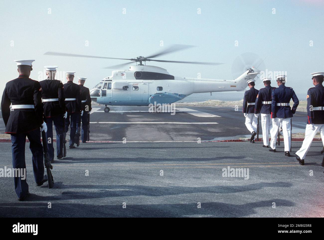A joint U.S.-Philippine Marine honor guard marches in formation as an SA-330 Puma helicopter transporting Philippine President Corazon Aquino arrives on base. Base: Naval Station, Subic Bay State: Luzon Country: Philippines(PHL) Stock Photo