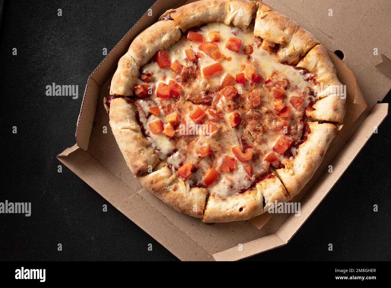 Pizza with tomatoes and mozzarella lies in a brown paper box. Pizza