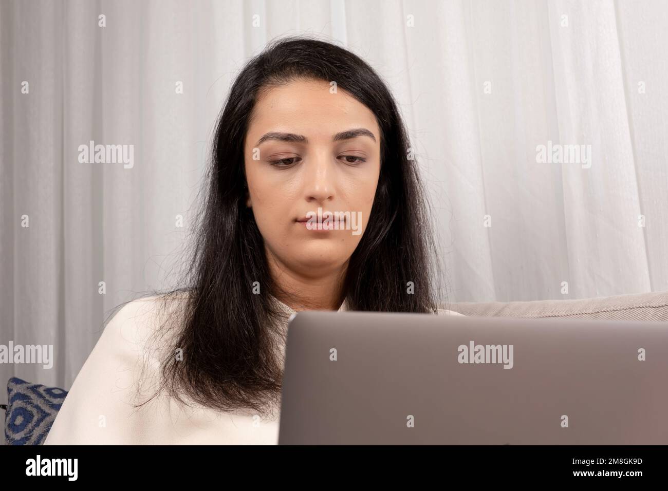 Woman using laptop. Sitting on couch at home. Shopping, chatting, working, online in social media, watching movie, freelancer, computer coding. Stock Photo
