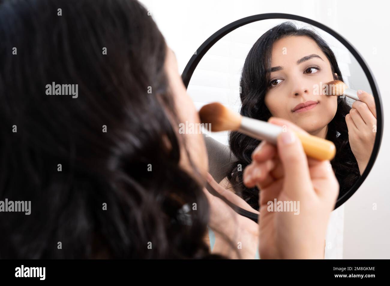 Charming beautiful dark hair woman putting night make up. Holding brush applying blusher or foundation powder. Professional cosmetics concept idea. Stock Photo