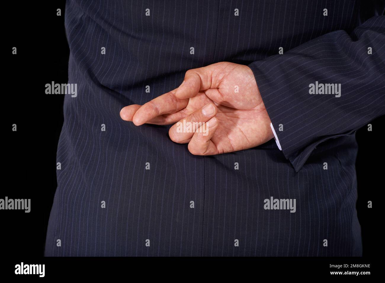 Telling lies. Cropped view of a man in a suit wth his fingers crossed behind his back. Stock Photo