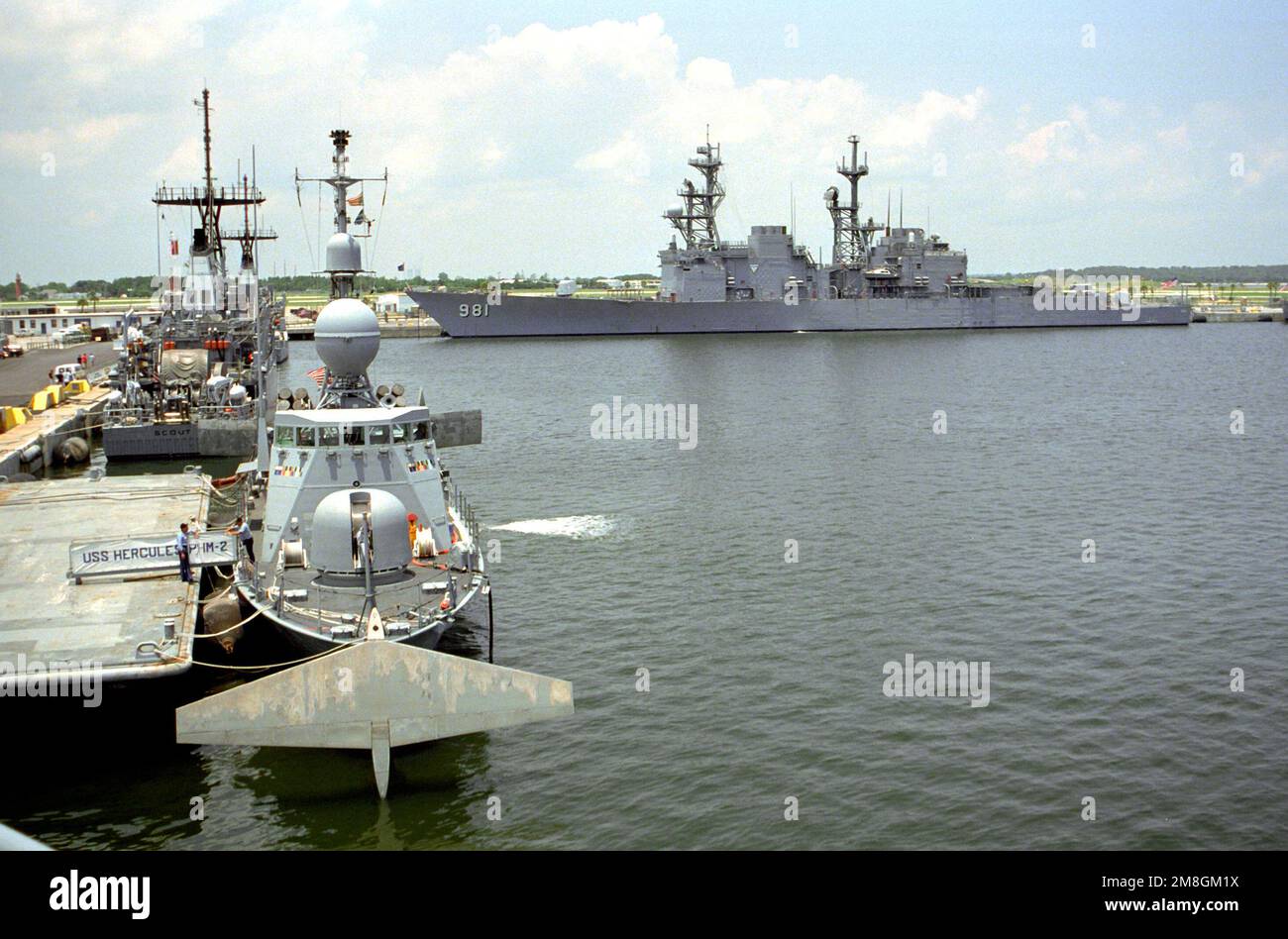 A bow view of the patrol combatant hydrofoil USS HERCULES (PHM-2) moored to a pier, with the mine countermeasures ship USS SCOUT (MCM-8) moored behind. The destroyer JOHN HANCOCK (DD-981) is moored in the background. Base: Naval Station, Mayport State: Florida(FL) Country: United States Of America (USA) Stock Photo