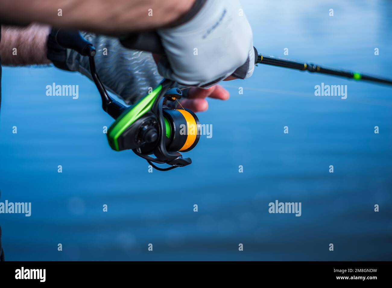 The fisherman holds a spinning rod in his hands. Angler with spinning rod  and fishing reel. Hands and spinning on the background of water. Blue water  Stock Photo - Alamy