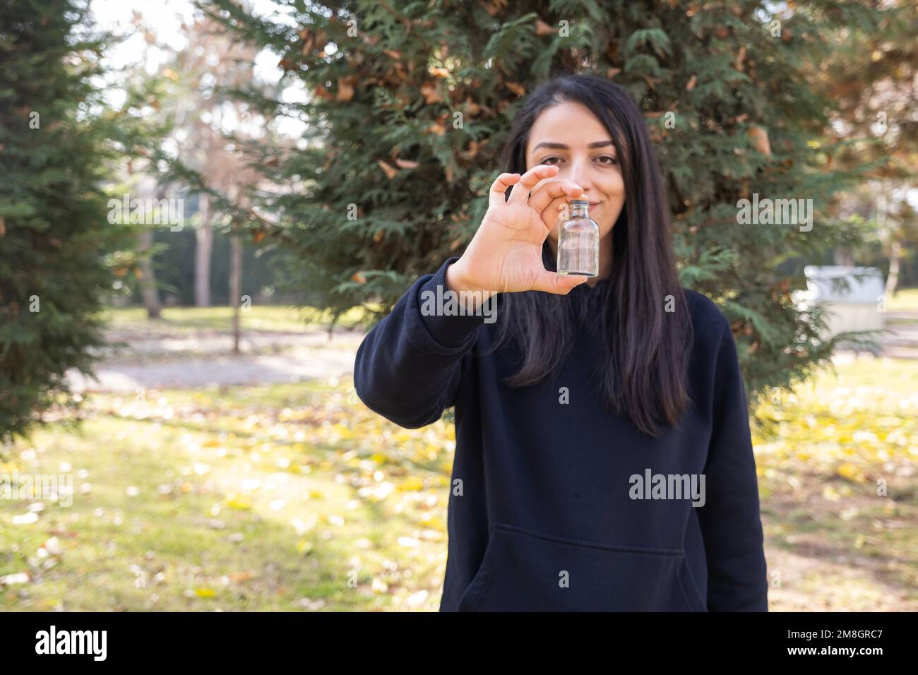 Woman holding and showing empty medicine pills bottle. Autumn forest or park background. Smiling pretty lady recommending vitamin supplements mock up. Stock Photo