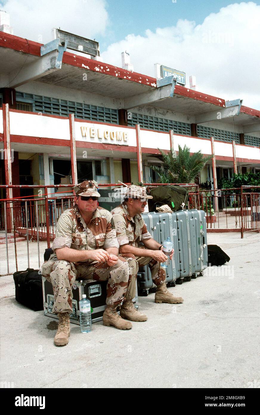 Photographer's Mate 2nd Class Dennis Dodd, left, and CHIEF Warrant Officer 4 Clyde Dunn, members of the Navy Broadcasting Service (NBS), wait for transportation in front of a terminal building at the Mogadishu International Airport during the multinational relief effort Operation Restore Hope. Subject Operation/Series: RESTORE HOPE Base: Mogadishu Country: Somalia (SOM) Stock Photo