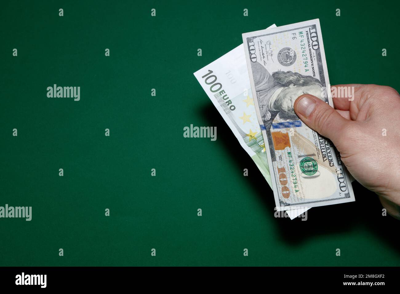 100 dollar and 100 Euro bills holds in hand on green background 100