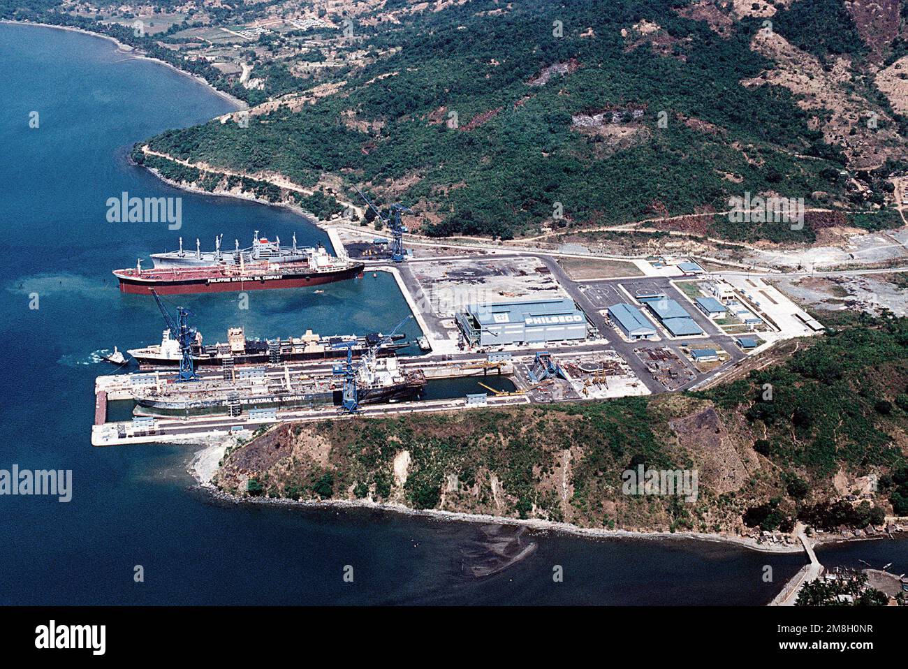 A view of four ships moored at the PHILSECO commerical ship repair facility. The ships are , from top to bottom, the cargo ship SANTA VICTORIA (T-AK-1010), a Philippine National Oil Company tanker, the barge cargo ship AUSTRAL RAINBOW (T-AKB-2046), and the Philippine National Oil Company tanker SULTAN KUDARAT, currently undergoing repairs. Base: Naval Station, Subic Bay State: Luzon Country: Philippines (PHL) Stock Photo