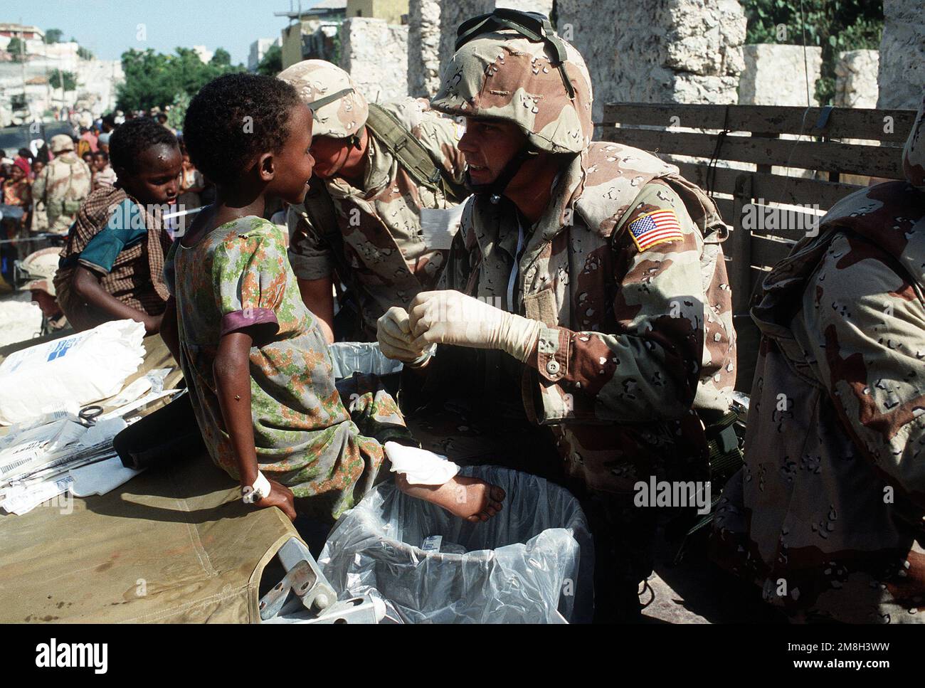 A Navy corpsman serving with Combat Service Support Detachment 15 talks with a Somali girl while treating her feet. He is participating in a medical civic action program being conducted during the multinational relief effort Operation Restore Hope. Subject Operation/Series: RESTORE HOPE Base: Mogadishu Country: Somalia (SOM) Stock Photo