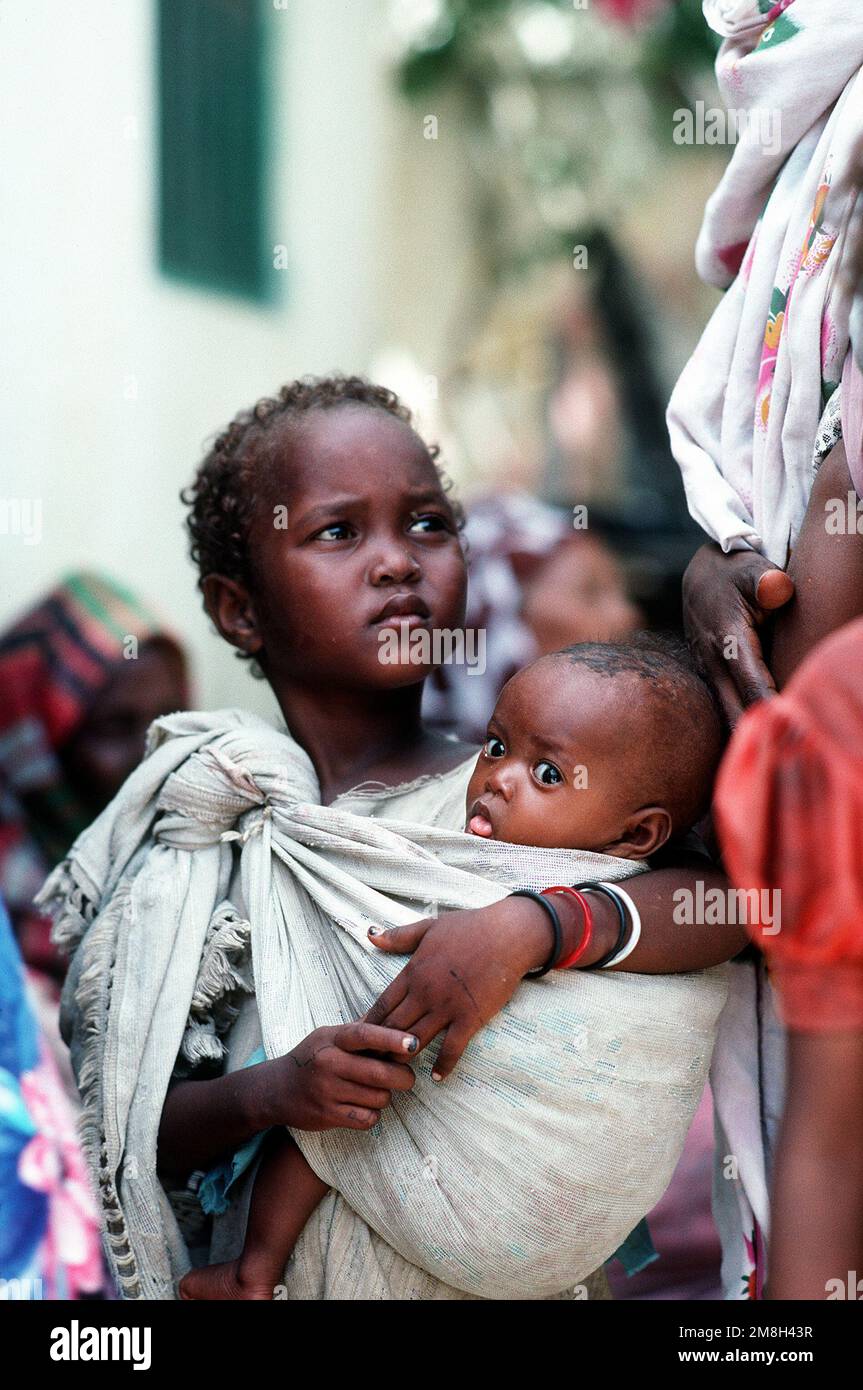A Somali girl holds an infant while waiting to be examined by a Navy corpsman. Combat Service Support Detachment 15 (CSSD-15) is conducting a medical civic action program in the streets of the city during the multinational relief effort Operation Restore Hope. Subject Operation/Series: RESTORE HOPE Base: Modadishu Country: Somalia (SOM) Stock Photo
