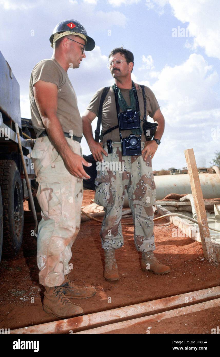 CHIEF Photographer's Mate Rober Sasek, assigned to the Joint Information Bureau, talks with a member of Naval Construction Battalion 1 (NMCB-1) participating in a water well drilling project during the multinational relief effort Operation Restore Hope. The well, near Bale Dogle, is intended to supply an old Soviet air base being used by U.S. and Moroccan personnel participating in the operation. Subject Operation/Series: RESTORE HOPE Country: Somalia (SOM) Stock Photo