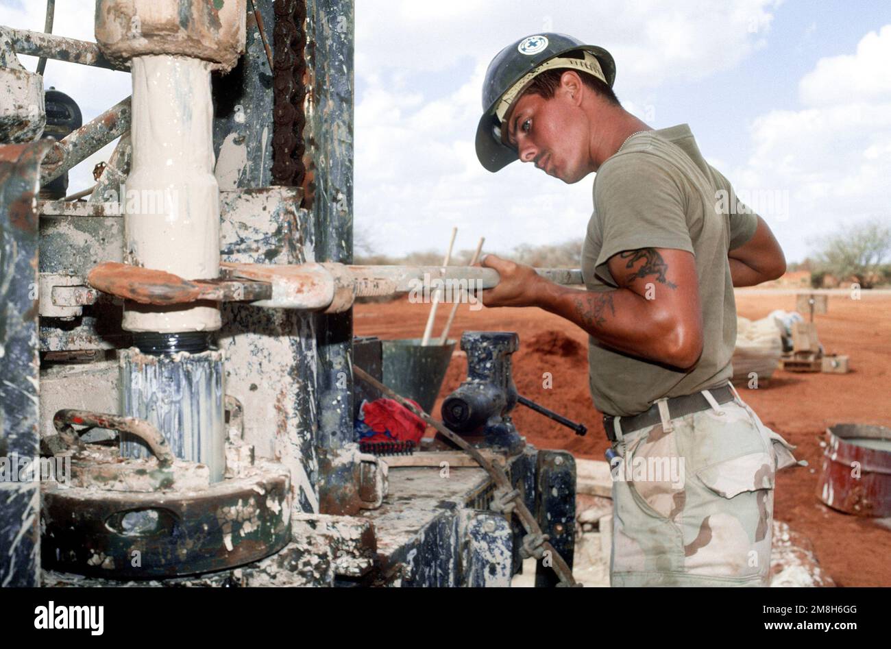 A member of Naval Mobile Construction Battalion 1 (NMCB-1) holds a section of drill shaft with a wrench while working on a mobile drilling rig being used to drill a water well. The well, near Bale Dogle, is intended to supply an old Soviet air base being used by U.S. and Moroccan personnel participating in the operation. Subject Operation/Series: RESTORE HOPE Country: Somalia (SOM) Stock Photo