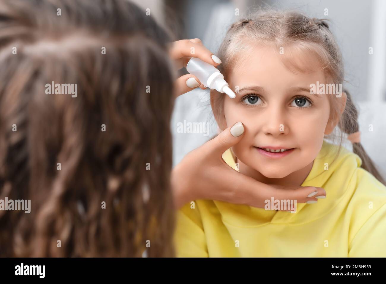 Mother putting drops in her little daughter's eye at home, closeup