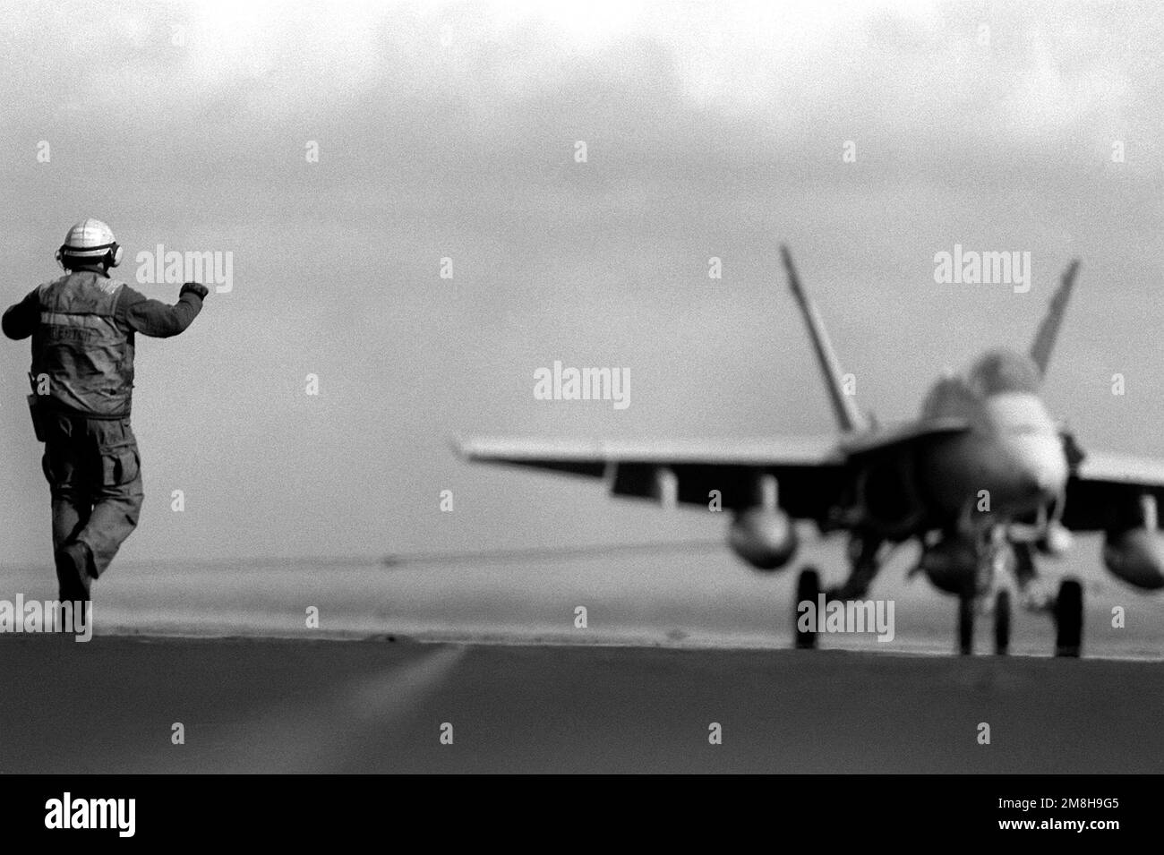 A flight deck crew member signals to the pilot of an F/A18