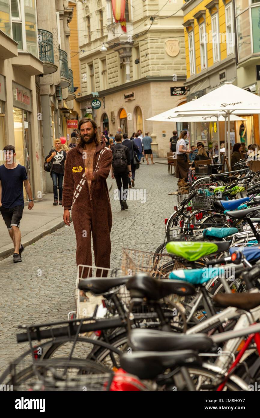 A shopping street with a lot of bicycles lined up as pedestrians walk by, one is wearing a Wookie onesie. Graz, Austria Stock Photo